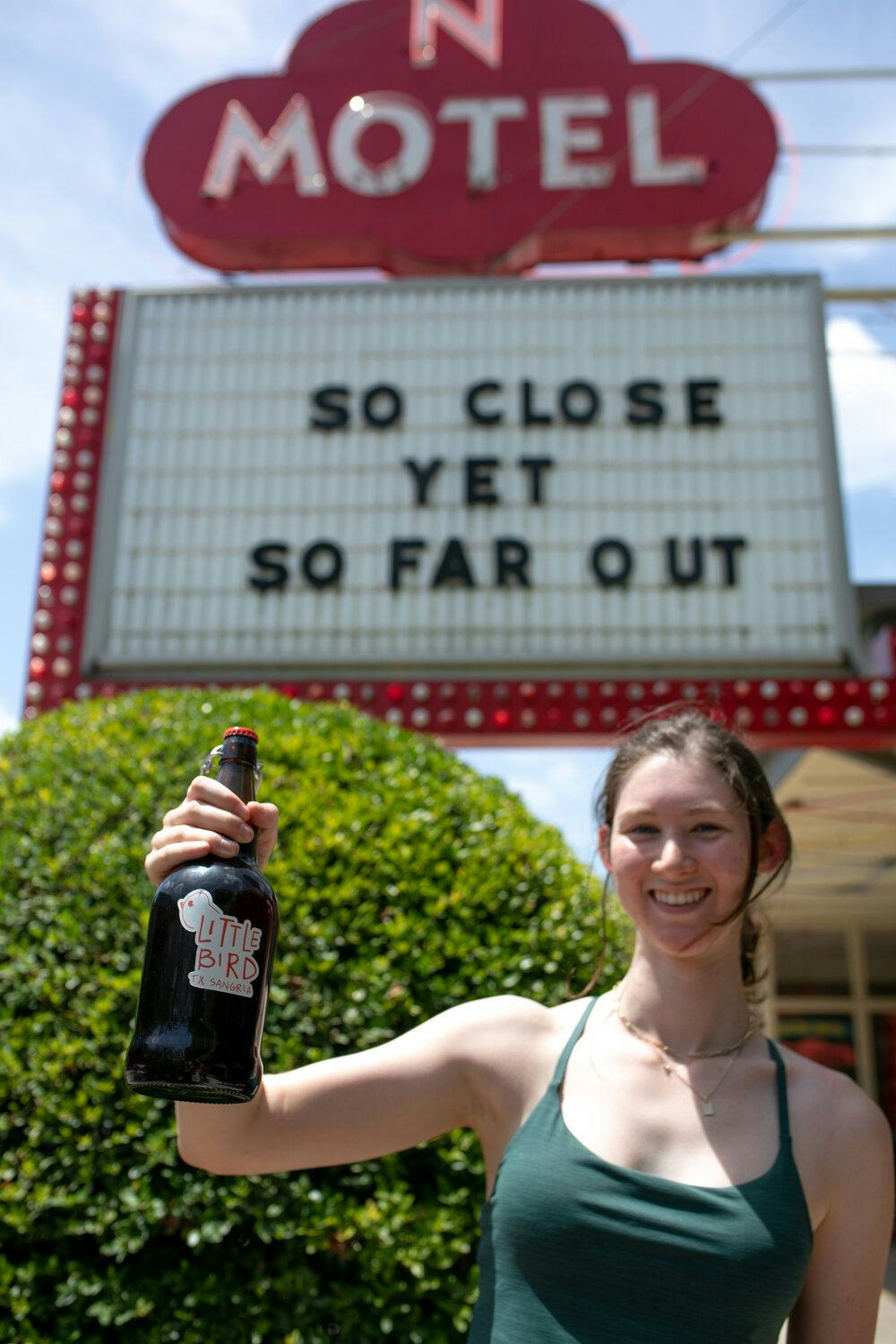 Ashley Deutser standing outside smiling and holding a bottle of Little Bird TX Sangria.
